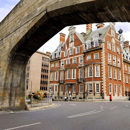 The Grand, York Hotel Exterior photo The photo depicts a street scene featuring a large, arched stone bridge in the foreground. Beneath the arch, there's a view of a curved road. To the right is a prominent brick building with a distinctive architectural style, characterized by multiple