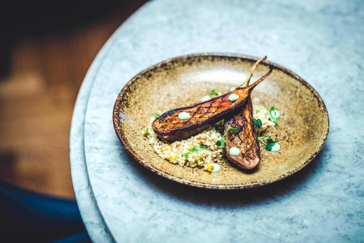 The Grand, York Hotel Exterior photo The photo depicts a beautifully arranged plate featuring two grilled or roasted pieces of eggplant (or a similar vegetable), garnished with small dollops of sauce on top. The eggplant pieces are placed on a bed of grains or a salad, which includes bi