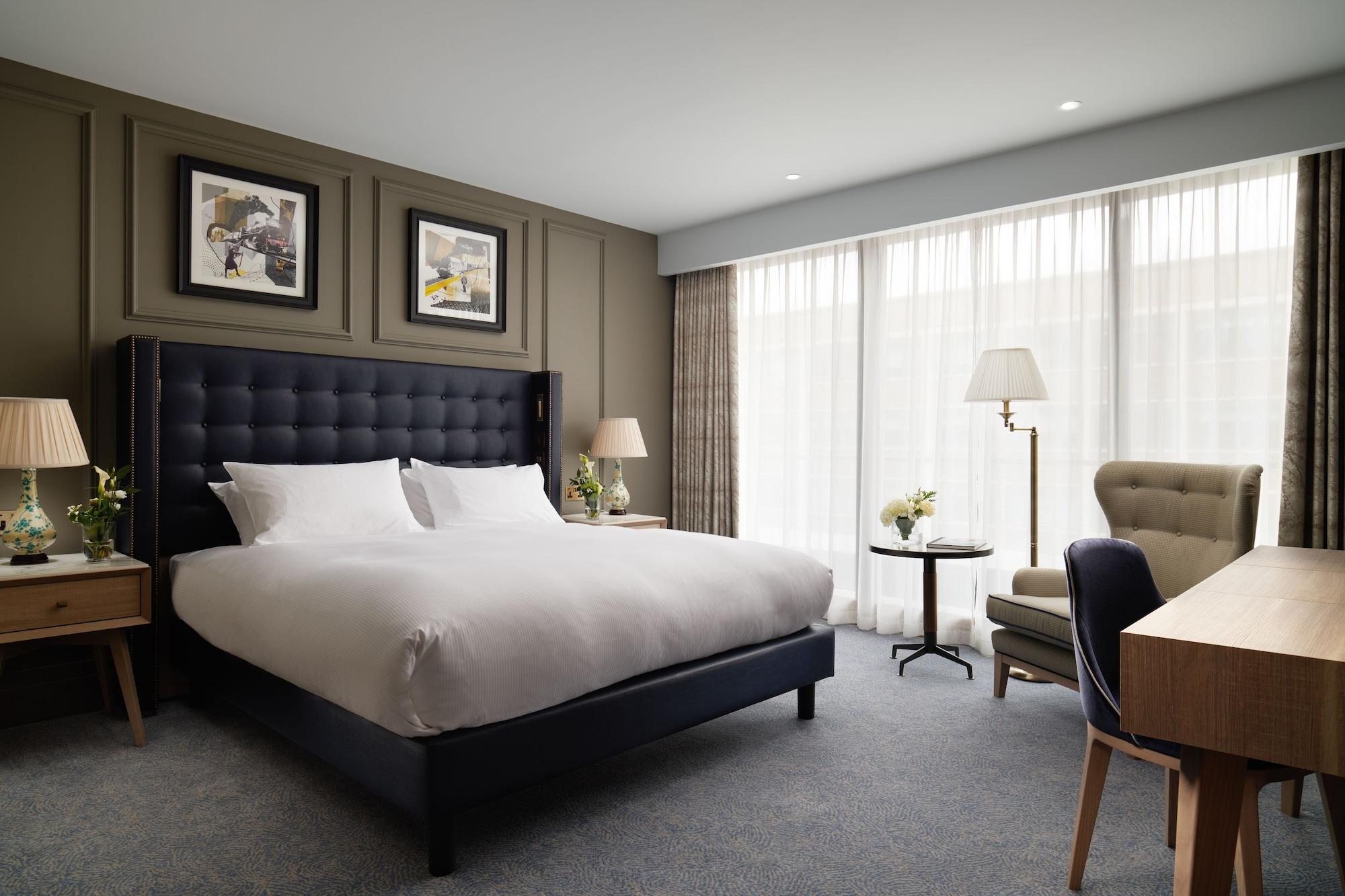 The Grand, York Hotel Exterior photo The photo shows a stylish hotel room featuring a large bed with white linens and a dark headboard. There are two framed artworks on the wall above the bed. To the side, there's a small round table with a flower arrangement, along with a comfortable a