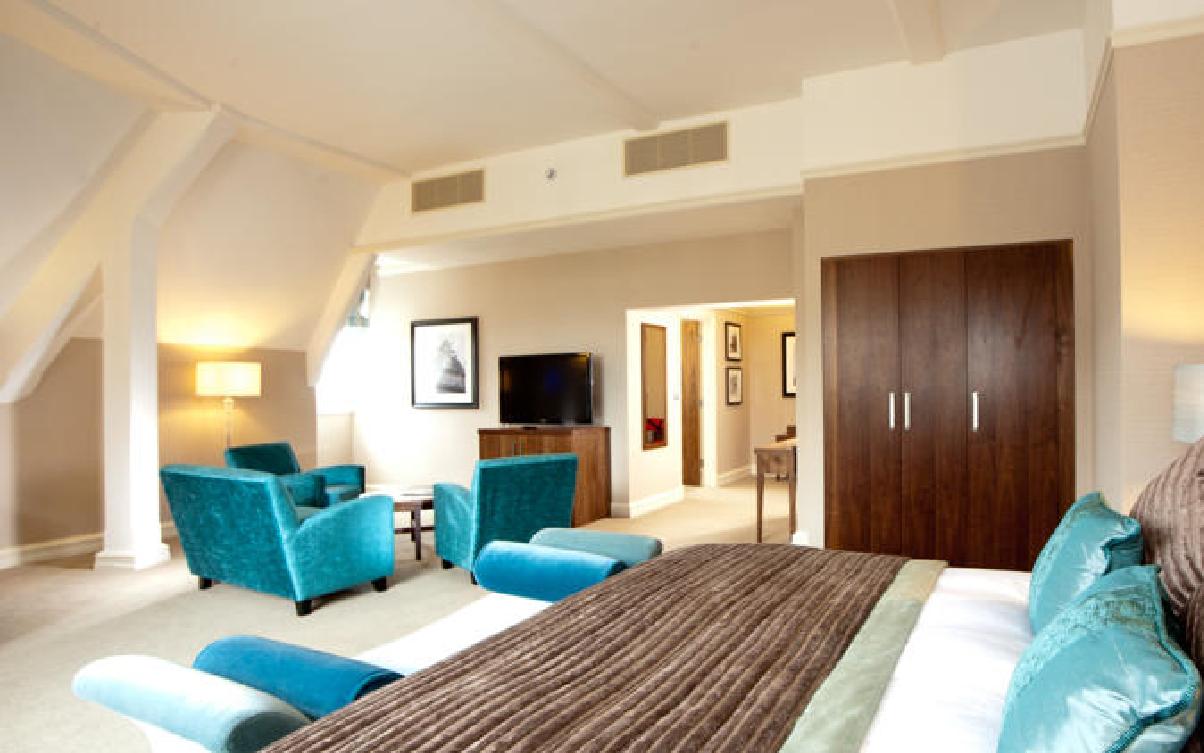 The Grand, York Hotel Exterior photo The photo shows a spacious hotel room or suite. The decor features a mix of modern and comfortable furnishings. 

In the foreground, there's a large bed with a textured brown bedspread. To the sides, there are plush armchairs in a turquoise color, co