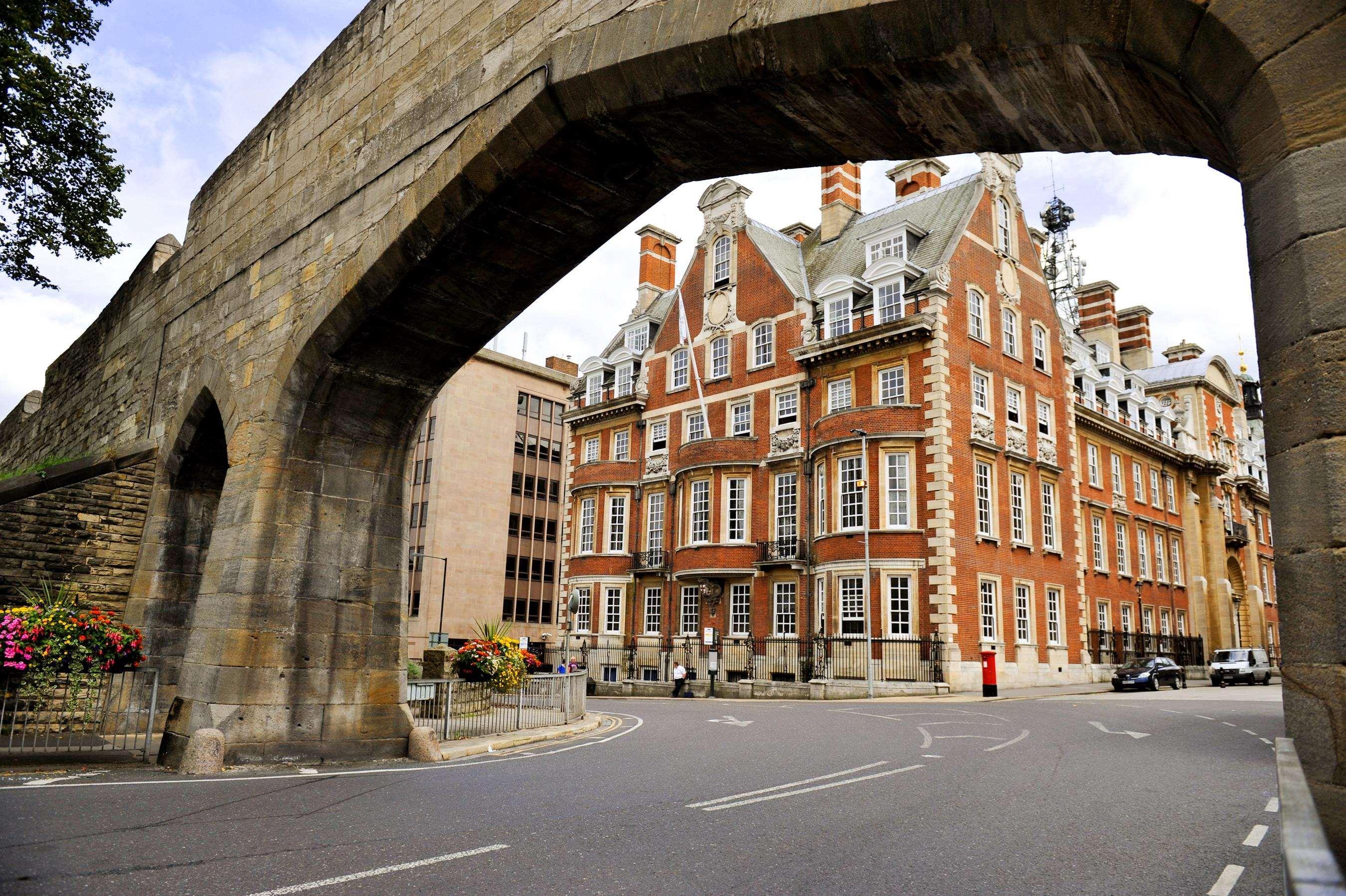The Grand, York Hotel Exterior photo The photo depicts a street scene featuring a large, arched stone bridge in the foreground. Beneath the arch, there's a view of a curved road. To the right is a prominent brick building with a distinctive architectural style, characterized by multiple